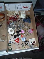 Box of assorted necklaces and earrings showing various bead styles, chains, and clip-on earrings.