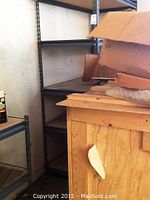 Side view of gray metal shelving unit against wall, showing five shelves and some stains on them.