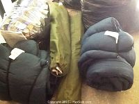 Two sleeping bags, two folded cots in carrying bags, one comforter wrapped in plastic