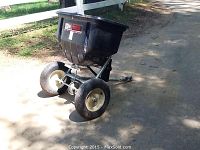 Side view of the spreader showing black plastic hopper, two rubber wheels and metal frame.