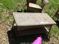 Outdoor photo of rectangular wicker coffee table with lower shelf, on grass, showing overall shape and condition