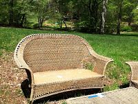 Full front view of the wicker sofa outdoors on grass showing curved backrest and armrests.