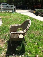 Side view of a vintage wicker chair showing curved armrests and backrest with metal legs in outdoor setting.
