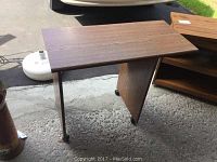 Faux wood side table shown from a top angle displaying main surface and single leg with casters.