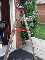 Front view of the wooden ladder showing the 5 steps, red metal fold-out bar and red paint tray at the top with paint stains.