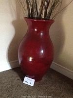 Photo showing large burgundy ceramic vase with flared rim and rounded body placed against wall.