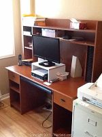 Full view of wood finish computer desk with hutch showing shelving and drawer, with electronic accessories on the desk surface.