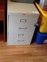Front view of light gray metal filing cabinet showing two drawers with handles and attached keys in lock.