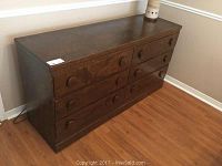 Full view of brown stained wooden dresser with six drawers, showing overall shape and surface condition.
