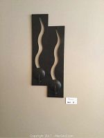 Full view of the black metal wall decor mounted on a light-colored wall, showing two rectangular panels with wavy cut-outs and circular elements at the bottom.