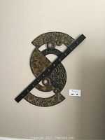 Front view of abstract metal wall art sculpture with circular segments, textured patterns, and a diagonal black bar with studs.