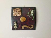 Front view of the metal abstract art showing textured and decorative raised elements on a burgundy background.