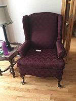 Front-facing view of the burgundy fabric wing chair highlighting the upholstery and carved wooden legs.