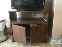 Cart shown with doors open revealing interior storage space under the pull-out shelf, microwave placed on top.