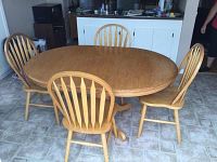 Full view of oval oak pedestal dining table with 4 matching chairs arranged around it in a room with tiled floor.