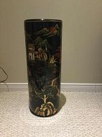 Full view of the tall cylindrical black vase showing the intricate scenic painting of mountains, trees, and a building.