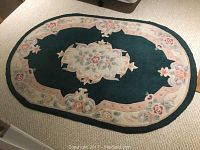 Large green floral oval rug laid flat on carpeted floor