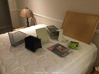Various office supplies including cork board, accordion file divider, metal organizer, white stand holder, ink cartridge, and plastic page protectors on bed