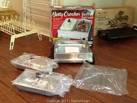 Buffet server components displayed including warming base, two trays, and plastic lids wrapped in original packaging on a wooden surface.