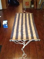Full view of the canvas hammock laid out on wooden floor showing striped pattern and ropes extending from wooden spreaders