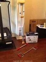 Photo showing pair of silver crutches with yellow padding, red handled arm exerciser chains on floor, and boxed Drive exercise peddler behind