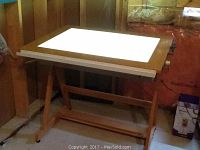 Full view of wooden illustrators drawing desk with illuminated top panel, wood frame and legs.