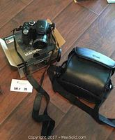 Fujifilm FinePix S2950 camera on box beside Case Logic camera bag, showing front angle and strap.