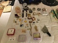 Wide view showing the assortment of costume jewellery spread out on a surface including watches, earrings, rings, bracelets, and jewellery boxes.
