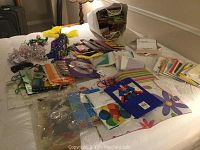 Overall view of assorted gift bags, occasion cards, ribbons, bows, beads, and a light-up bow tie spread on a bed.