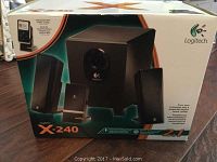 Box front showing Logitech X-240 music center including two satellite speakers, subwoofer, and MP3 player cradle details