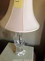 Clear glass lamp with a large white fabric shade and ornate metal base seen from front