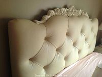 Side-angle view of ivory leather tufted headboard and part of wooden frame