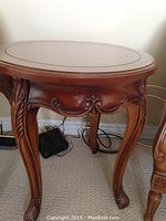 Front angled view of round solid wood side table showing carved legs and side details