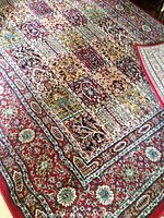 Angled view of the full carpet showing the detailed multicolored floral and geometric pattern with a dominant red border.