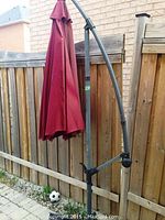 Full view of red outdoor umbrella attached to black metal stand with fence background on patio.
