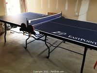 Full view of assembled blue EastPoint ping pong table in garage with net and paddles attached
