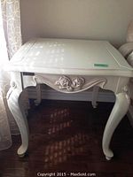Full view of cream-coloured solid wood end table with curved legs and carved rose pattern on apron.