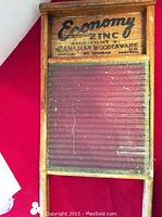 Full view of antique wooden framed washboard with Economy Zinc ribbed glass scrubbing surface against a red background.