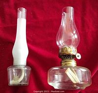 Two small glass oil lanterns on red background, one with frosted chimney, one with clear chimney and brass burner.