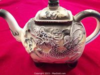 Front side of the ceramic teapot showing detailed raised dragon design with handpainted brown shading and textured scales.