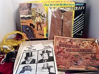 Lot overview showing the contents: a leather handbag kit with lacing, Al Stoneman carving book, leather hat patterns, and a Western leathercraft magazine.