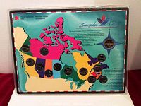 Photo shows set of commemorative coins on a colorful map of Canada in a plastic display case, with coins arranged over provinces. The map features bright colors and text marking 125th Anniversary.
