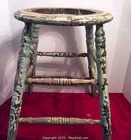 Front view of vintage wooden stool frame showing original chipped turquoise and brown paint on turned legs and stretchers.