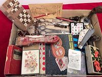 Overall view of box containing older scissors, keys, games, pocket knife, and miscellaneous items, showing various objects including wooden checkerboard and sliding tile game.