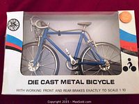 Die cast metal bicycle model in retail packaging showing front side and blue frame.