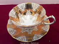 Close-up of the gold decorated bone china cup with ornate gold scrollwork inside and outside, scalloped rim and elegant handle.