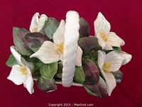 Top view of white bone china basket filled with white trillium flowers and green leaves.