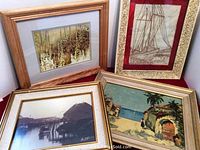 Four framed artworks leaning against a white wall showing a nature print, a sailboat sketch, a coastal painting, and a waterfront scene, all about 14 by 12 inches.