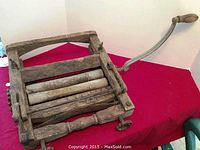 Side angle view showing entire wooden hand laundry wringer with metal side handle and wooden grip resting on red surface.