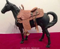 Black heavy metal horse figurine with tooled leather saddle on red background, side view showing saddle details.